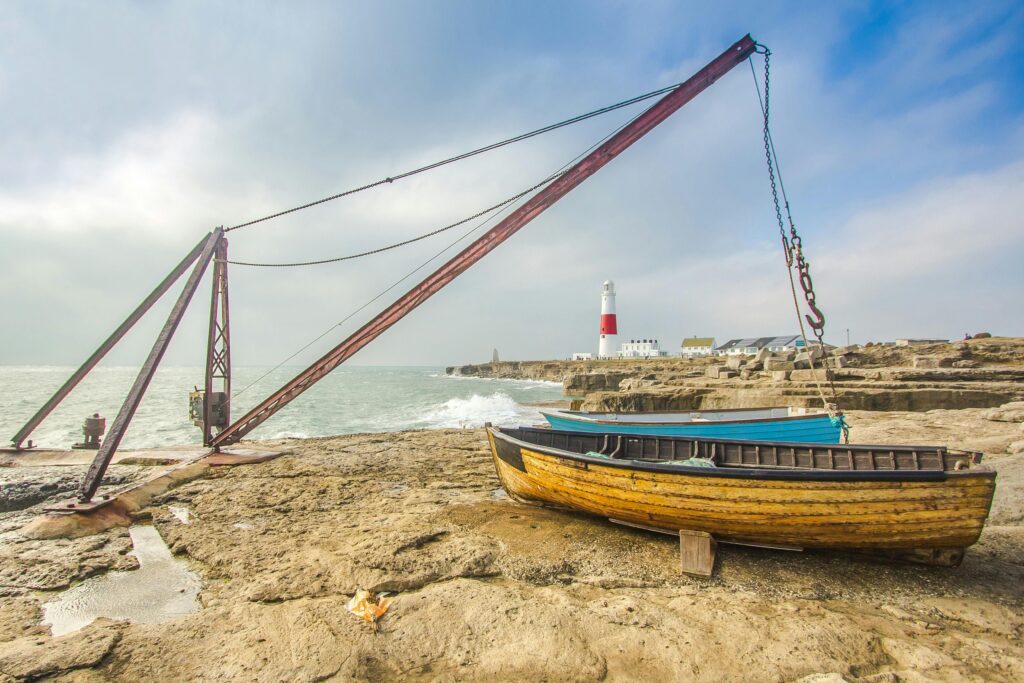 A peaceful seaside scene featuring a lighthouse, boats, and a crane on a rocky coast.